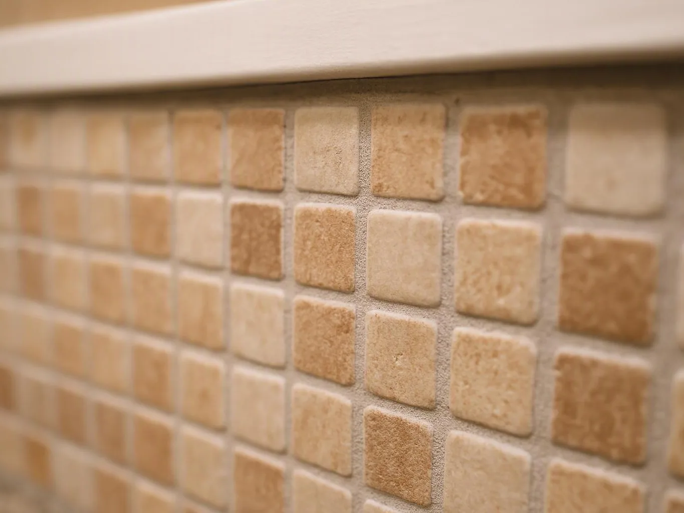 Close-up of beige square mosaic tiles on a wall with a white ledge above