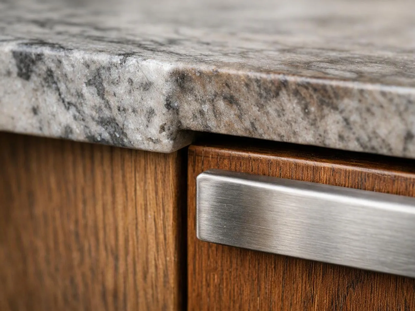 Close-up of a granite countertop over wooden cabinet doors with a brushed metal handle