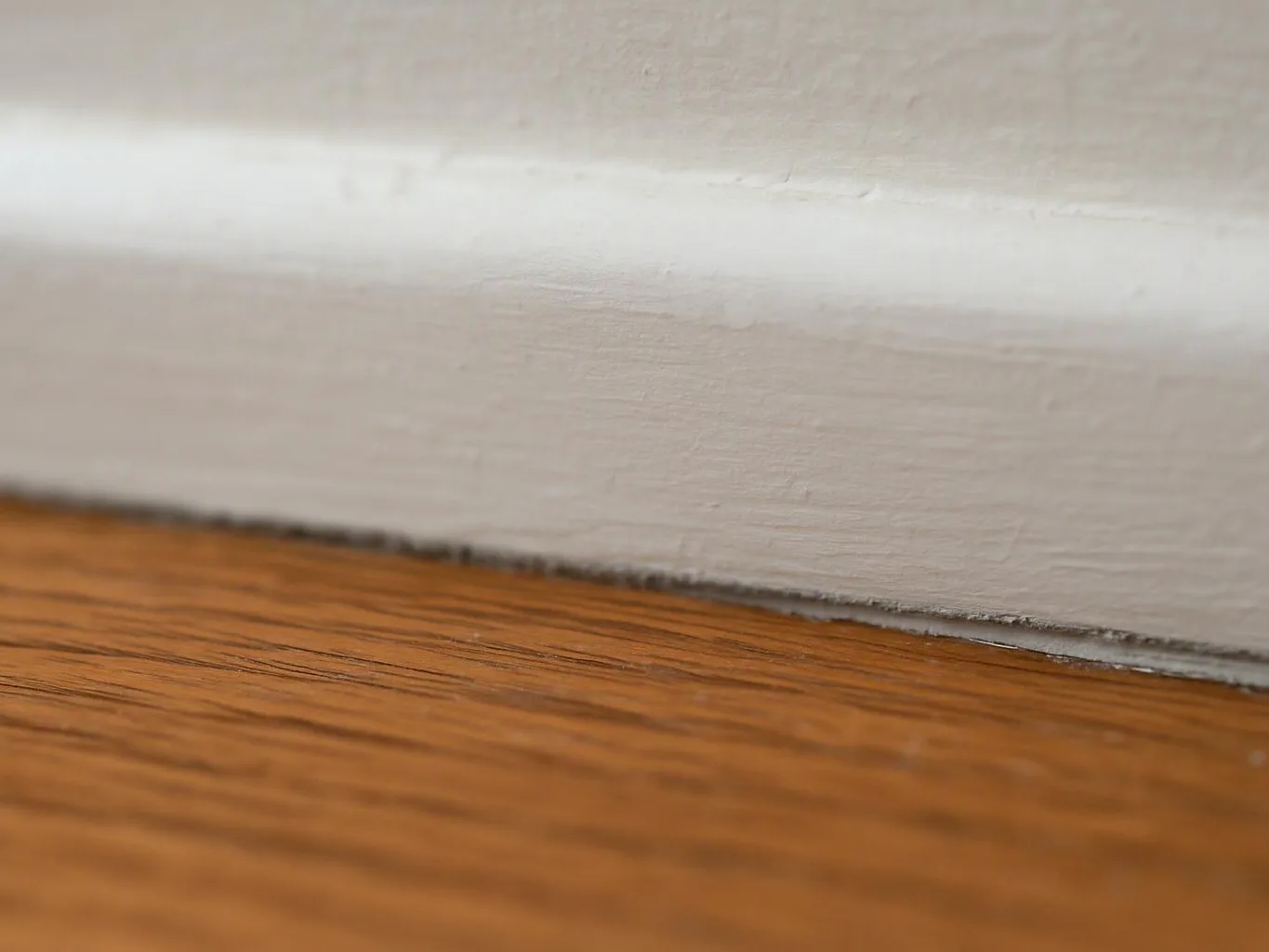Close-up of a white baseboard meeting a wood floor, with a narrow dark gap along the edge