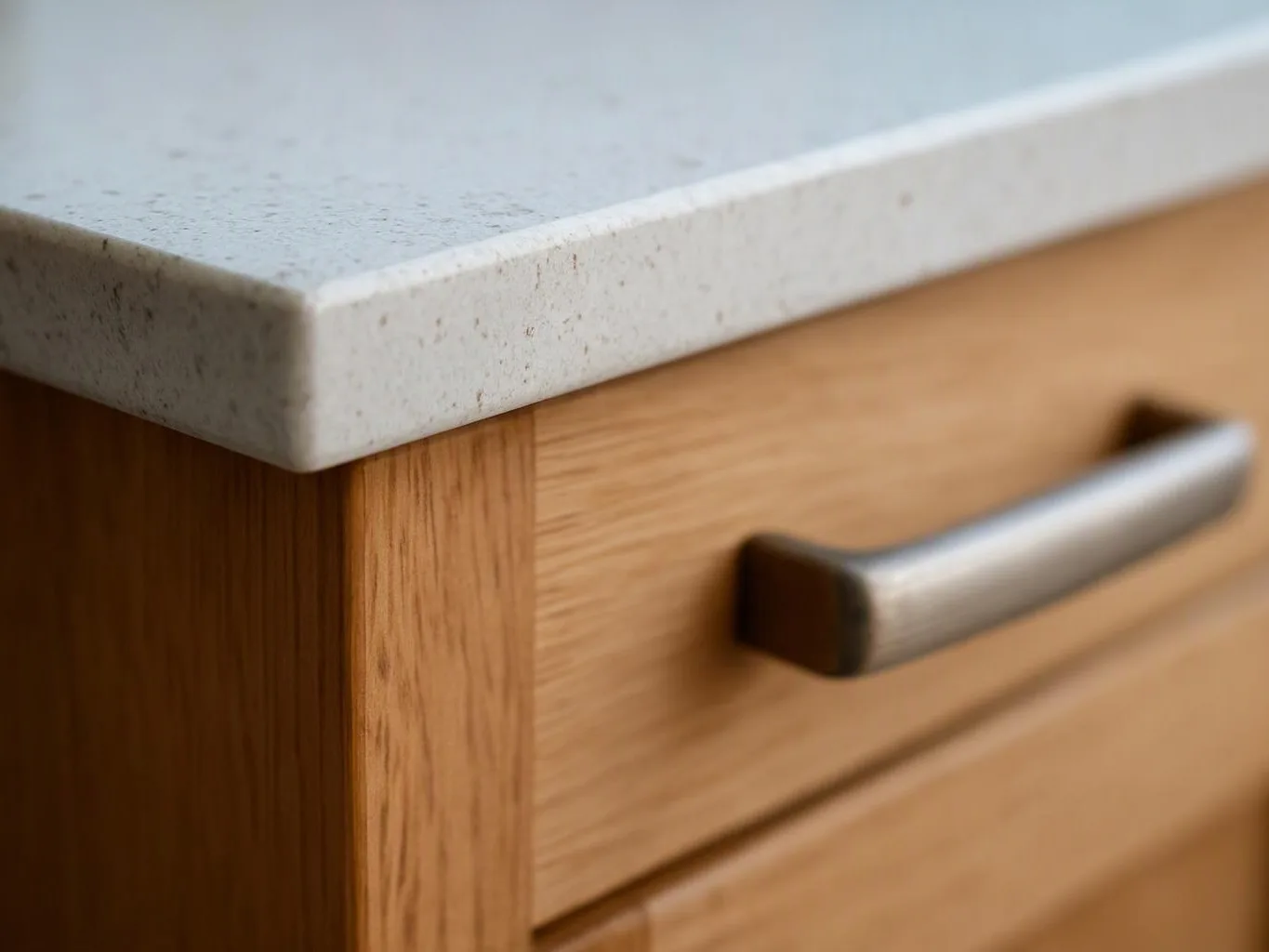 Close-up of a wooden drawer with a metal handle and a light stone countertop above it